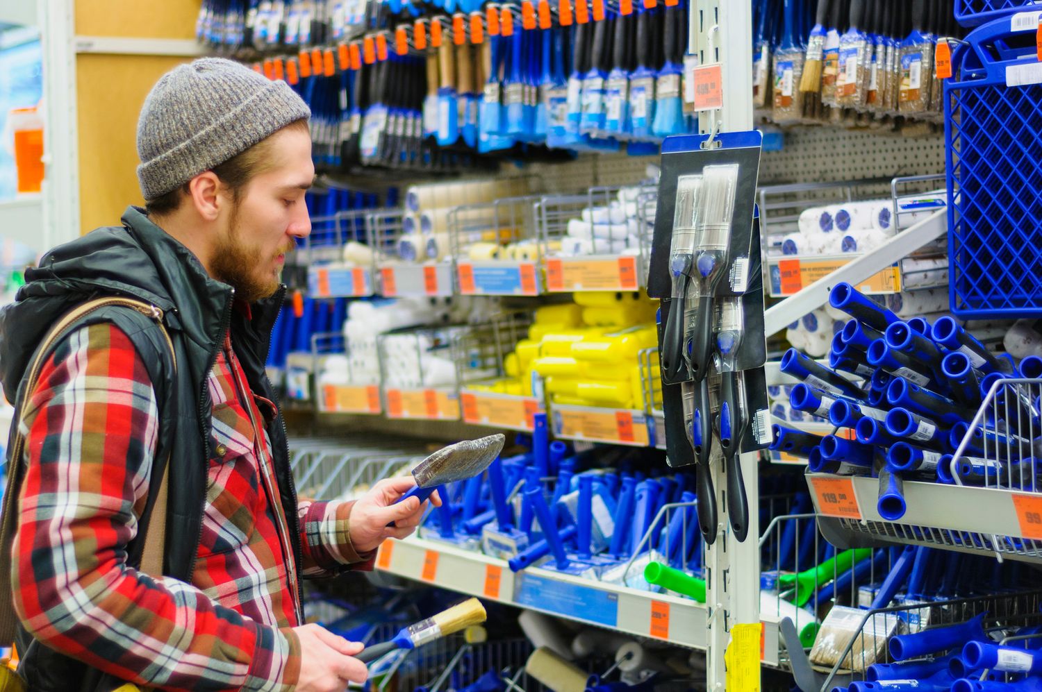 A young man chooses paintbrush in the hardware store