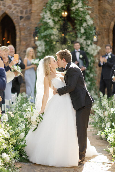 bride and groom kissing in aisle of wedding ceremony