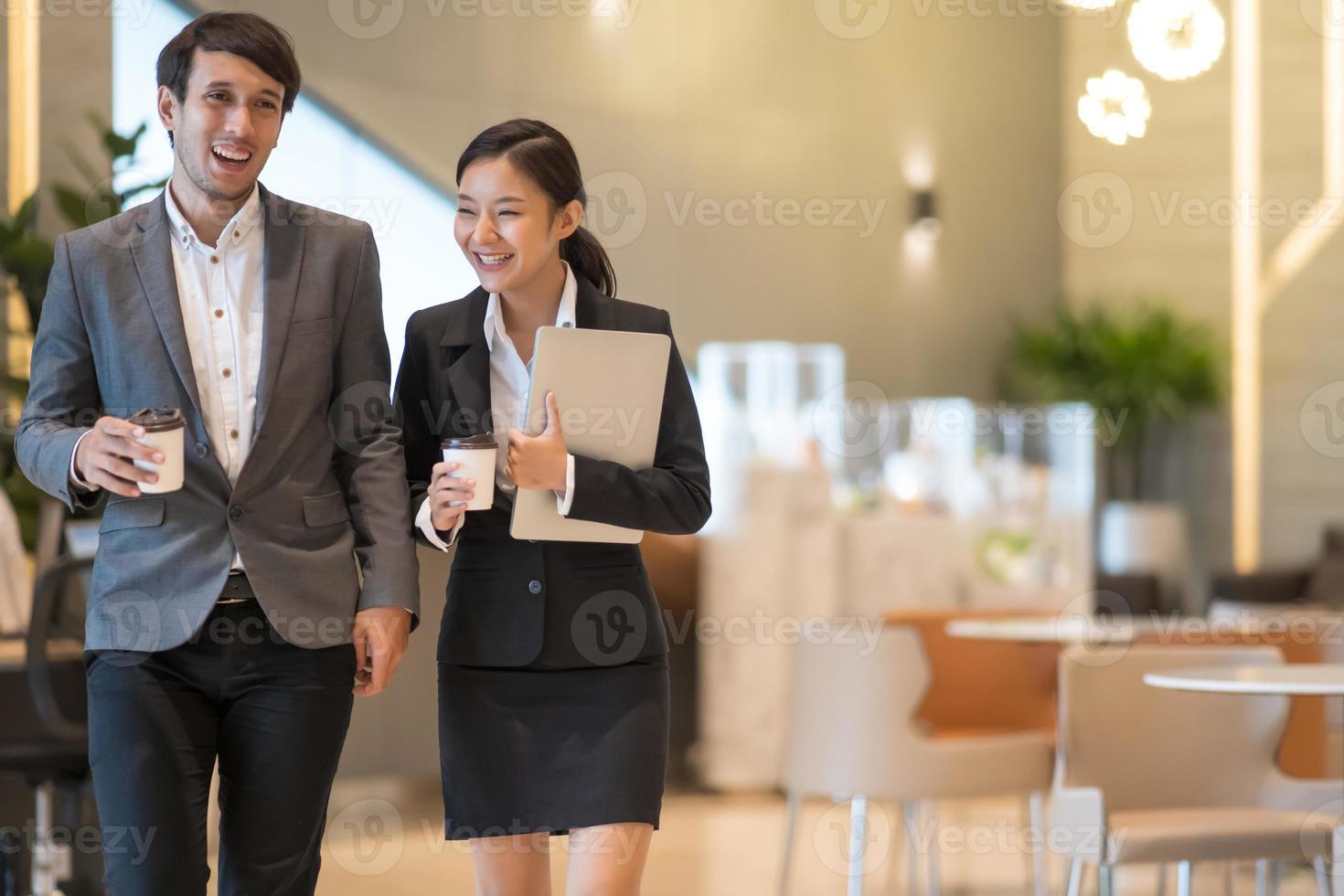 Asian business people  walking in office building. Young businessman and businesswoman talking when walking. photo