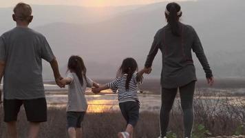 Rear view of family holding hands while strolling by the lake and watching the sunset. Happy family enjoying the beautiful view at sunset. video