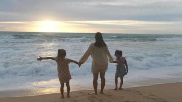 Happy Asian family of mother and daughters having fun playing on the beach during summer vacation at sunset. Summer family trip to the beach. travel and vacation concept. video