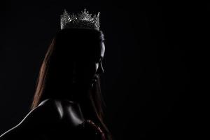 Portrait of Miss Pageant Beauty Contest in sequin Evening Ball Gown long dress with sparkle light Diamond Crown, silhouette low key exposure with curtain, studio lighting dark background dramatic photo