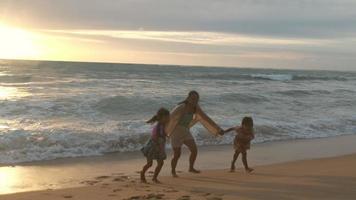 Happy Asian family of mother and daughters having fun playing on the beach during summer vacation at sunset. Summer family trip to the beach. travel and vacation concept. video