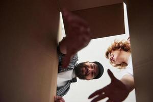 Bearded man trying to reach the item down of a box. Happy couple together in their new house. Conception of moving photo