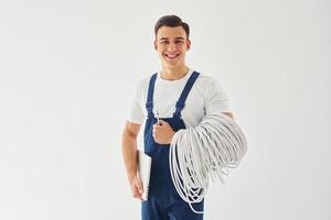 Holds cables, notepad and screwdriver. Male worker in blue uniform standing inside of studio against white background photo