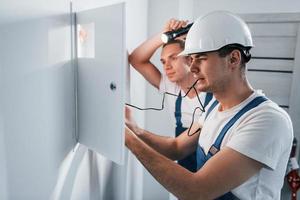 Two young male electricians works indoors together. Using flashlight photo