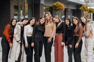 Group of smiling and happy teenage friends wearing casual clothes spending time together, posing and talking with each other near college building on autumn day. photo