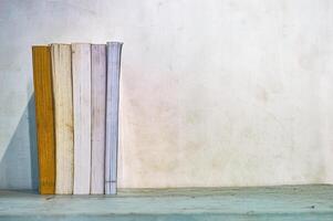 a collection of thick books neatly arranged standing on a table against a white wall background photo