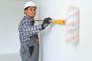 An Indian apartment repair worker paints a white wall with a roller. photo