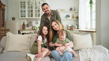 Happy family at home. Mother father two children daughters relaxing on sofa indoor. Mom dad parents baby girls kids relax playing having fun together. Family smiling laughing enjoying tender moment video