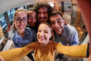 A diverse group of business professionals take a break from their tasks in a modern startup office to capture a creative selfie, showcasing teamwork and a vibrant workplace culture photo