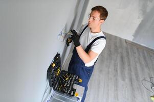 Electrician with screwdriver repairing power socket in room photo