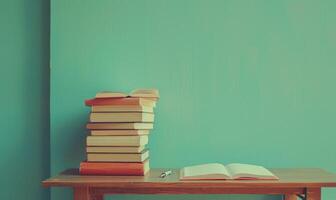 Stack of books on a wooden table with a pastel turquoise background, with an open notebook and pen photo