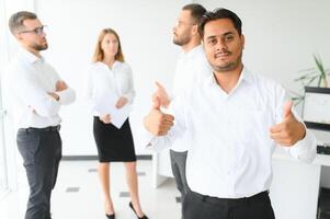 Portrait of smiling indian businessman standing in modern office on colleagues background photo