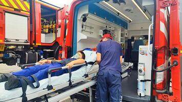 A teenage boy lies on a gurney in an ambulance, a rescue worker helps him and provides first aid. Saving the life of a small patient by an ambulance doctor. photo