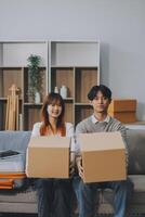 Young Asian couple relocating to a new house, joyfully packing and unpacking belongings. Expertise in moving, packing, togetherness, and creating a new home together. photo