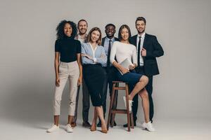 Happy young business team in formalwear looking at camera while standing on beige background photo