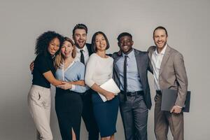 Happy young business team in formalwear embracing while standing on beige background photo