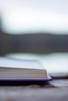 Open book with pages flipping in the wind. Reading on the lake wooden dock on autumn day. Learning enjoying tranquility of nature. Peaceful outdoor environment. Selective focus. Blurred background. photo