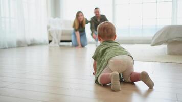 Happy family. Mother father looking at cute little toddler girl crawling on floor in bedroom. Infant baby resting playing with parents indoor at home. Mom dad newborn baby. Cute crawling child video