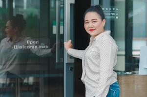 Shopping and small business owner , Businesswoman confidently opening door, her warm smile and stylish outfit scene captures moment of empowerment and positivity in modern setting photo