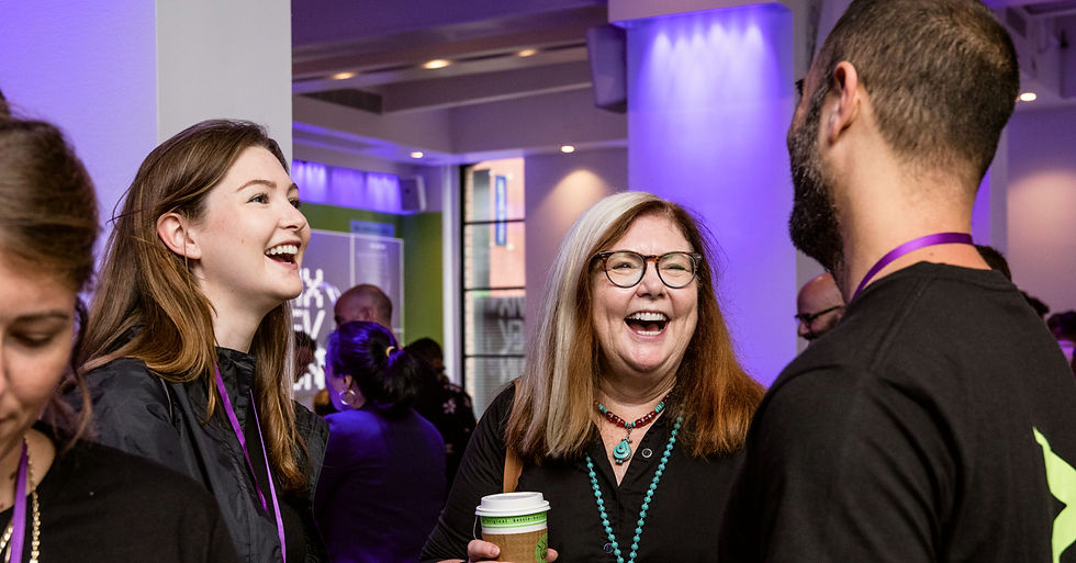 Two women and a man, all dressed in black, talk and laugh at a busy event.