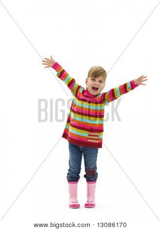 Happy little girl in colorful sweater, jeans and pink boots, laughing and waving. Isolated on white background.