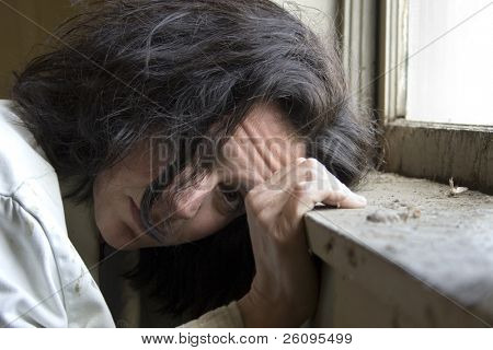 Thirty-eight year old woman looking out the window of impoverished home. Hopeless expression on face.