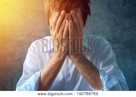 Hopeless depressive businessman in white shirt with roll up sleeves hands covering face crying in despair