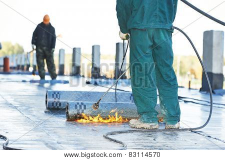 Roofer installing Roofing felt with heating and melting of bitumen roll by torch on flame during roof repair