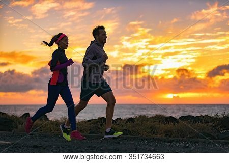 Running people training cardio together active friends jogging in early morning dawn sunrise on beach. Run fit couple runners woman and man running outdoor. Silhouettes of two athletes working out.