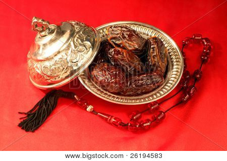 A silver bowl containing the finest dates, which are traditionally eaten in Arabia for Iftar to break the Ramadan fast at sundown, next to prayer beads.