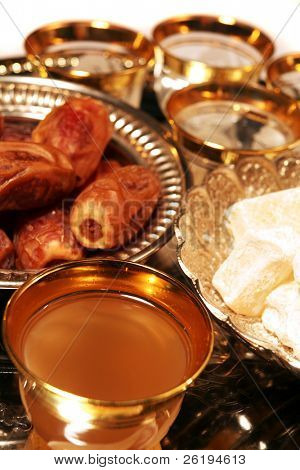 A cup of traditional green coffee (ghawa) with Turkish delight (raha haloum) and dates on a silver tray. Traditional Arab Ramadan fast-breaking treats.