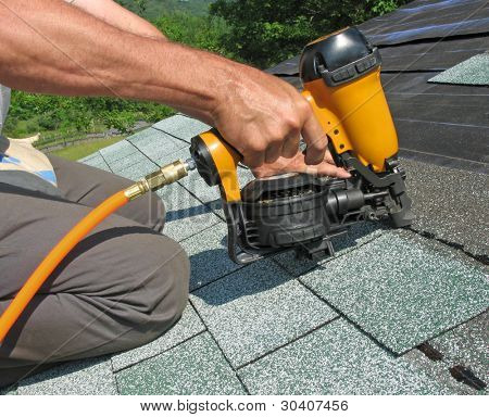 Carpenter uses nail gun to attach asphalt shingles to roof