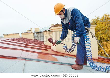 roofer builder worker with pulverizer spraying paint on metal sheet roof