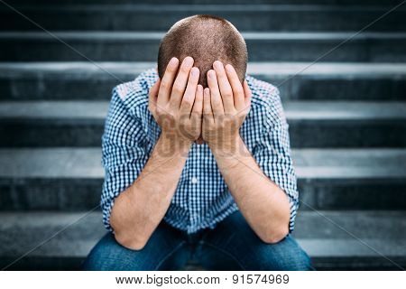 Outdoor Portrait Of Sad Young Man Covering His Face With Hands. Selective Focus On Hands