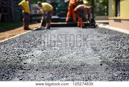 Team of Workers making and constructing asphalt road construction with finisher. The top layer of asphalt road on a private residence house driveway