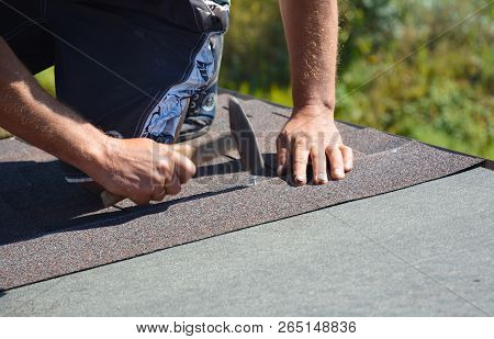 Roofer Installing Asphalt Shingles On House Construction Roof Corner With Hammer And Nails. Roofing 