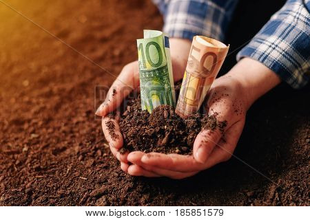 Hands with fertile soil and euro money banknotes female farmer handful of cultivated land that makes profit and steady income from sustainable agricultural activity like organic growth of crops