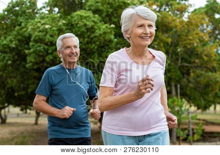 Senior couple running outside at park. Elderly man and old woman jogging together. Retired man and active woman exercising outdoor.