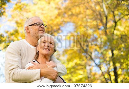 family, age, season and people concept - happy senior couple hugging over autumn trees background