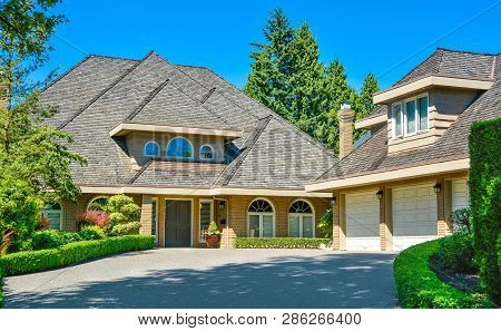 Residential House With Massive Roofs With Green Hedge At The Entrance On Blue Sky Background. Family