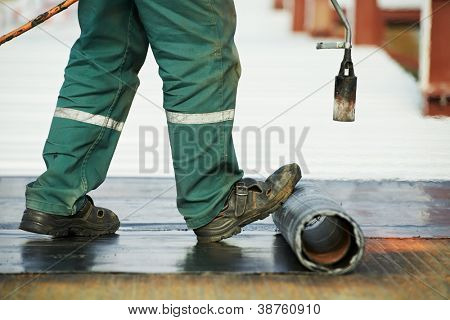 Roofer installing Roofing felt with heating and melting of bitumen roll by torch on flame during roof repair