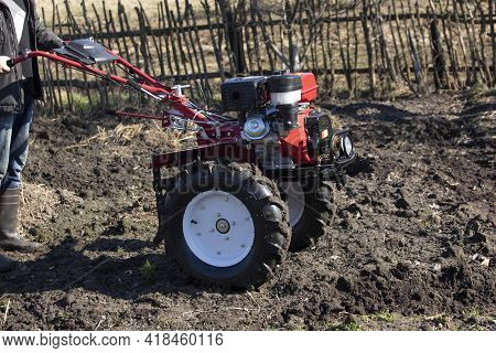 A Farmer Man Plows The Land With A Cultivator. Machinery Cultivator For Soil Cultivation In The Gard