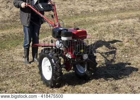 A Farmer Man Plows The Land With A Cultivator. Machinery Cultivator For Soil Cultivation In The Gard