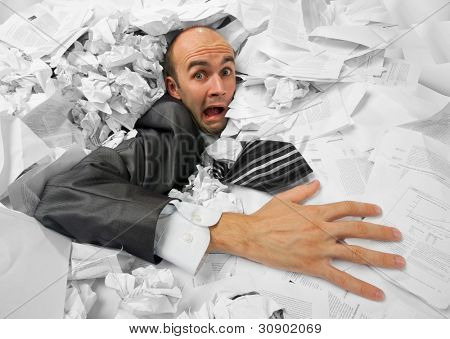 Businessman sinking in heap of documents and asking for help