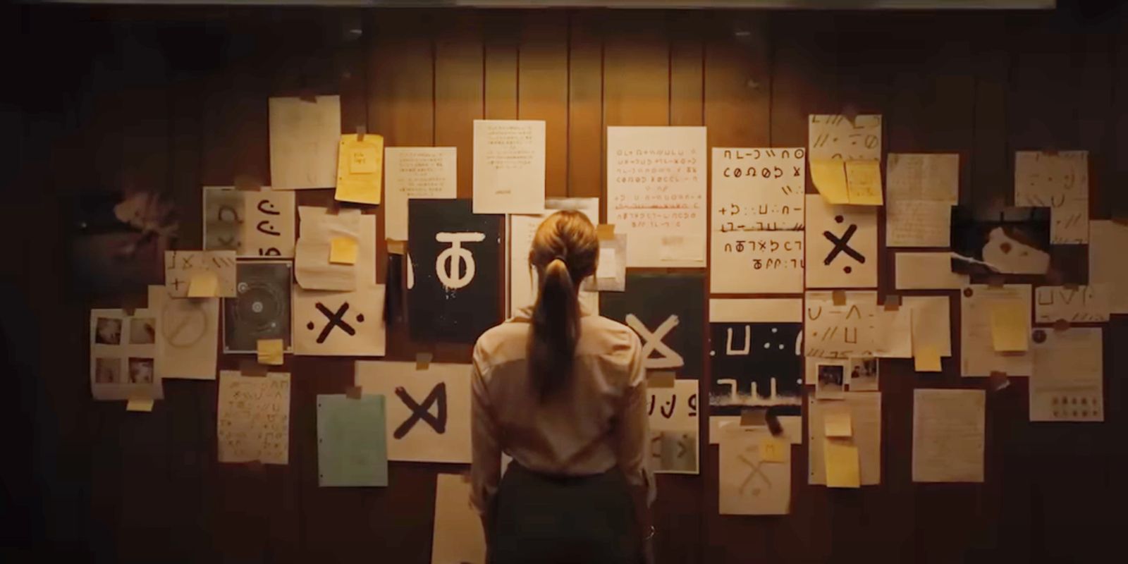 Woman looking at papers with weird symbol strewn over a wall in Longlegs