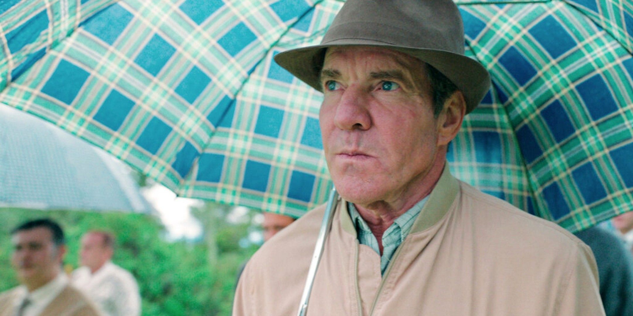 Dennis Quaid standing under an umbrella in The Long Game