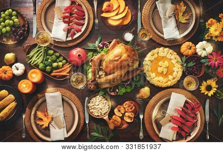 Thanksgiving celebration traditional dinner. Roasted turkey garnished with cranberries on a rustic style table decoraded with pumpkins, vegetables, pie, flowers and candles. Festive table setting