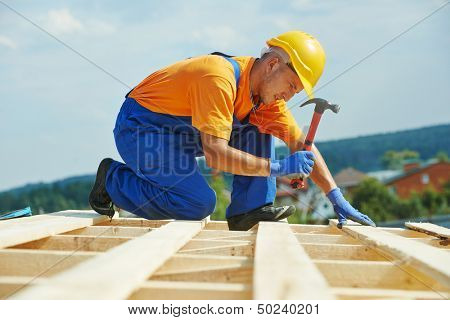 construction roofer carpenter worker nailing wood board with hammer on roof installation work